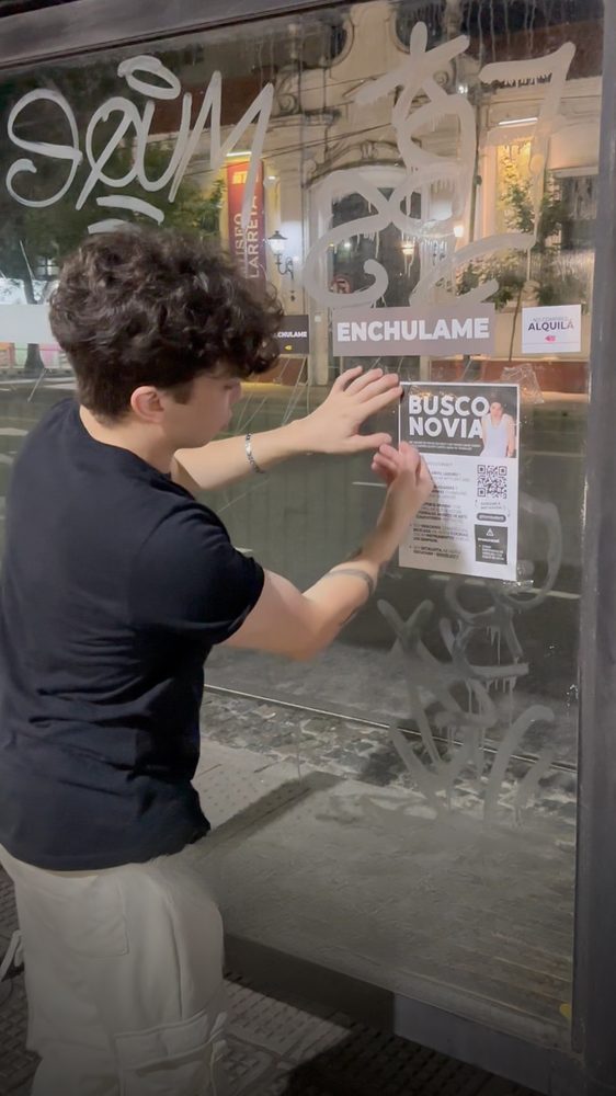 Tomás pegando un cartel de Busco novia en una parada de colectivo